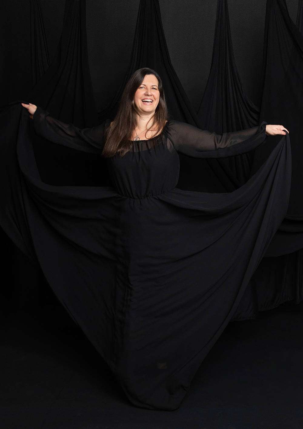kirsten Kirsten Landauer trägt ein schwarzes Kleid und lächelt mit ausgebreiteten Armen in die Kamera